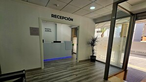 A hotel reception area with a reception desk labeled "RECEPCIÓN" and "HOSTAL ANNA." There is a potted plant near the entrance and a bench in the foreground. - Apartamentos Maja (Benidorm)