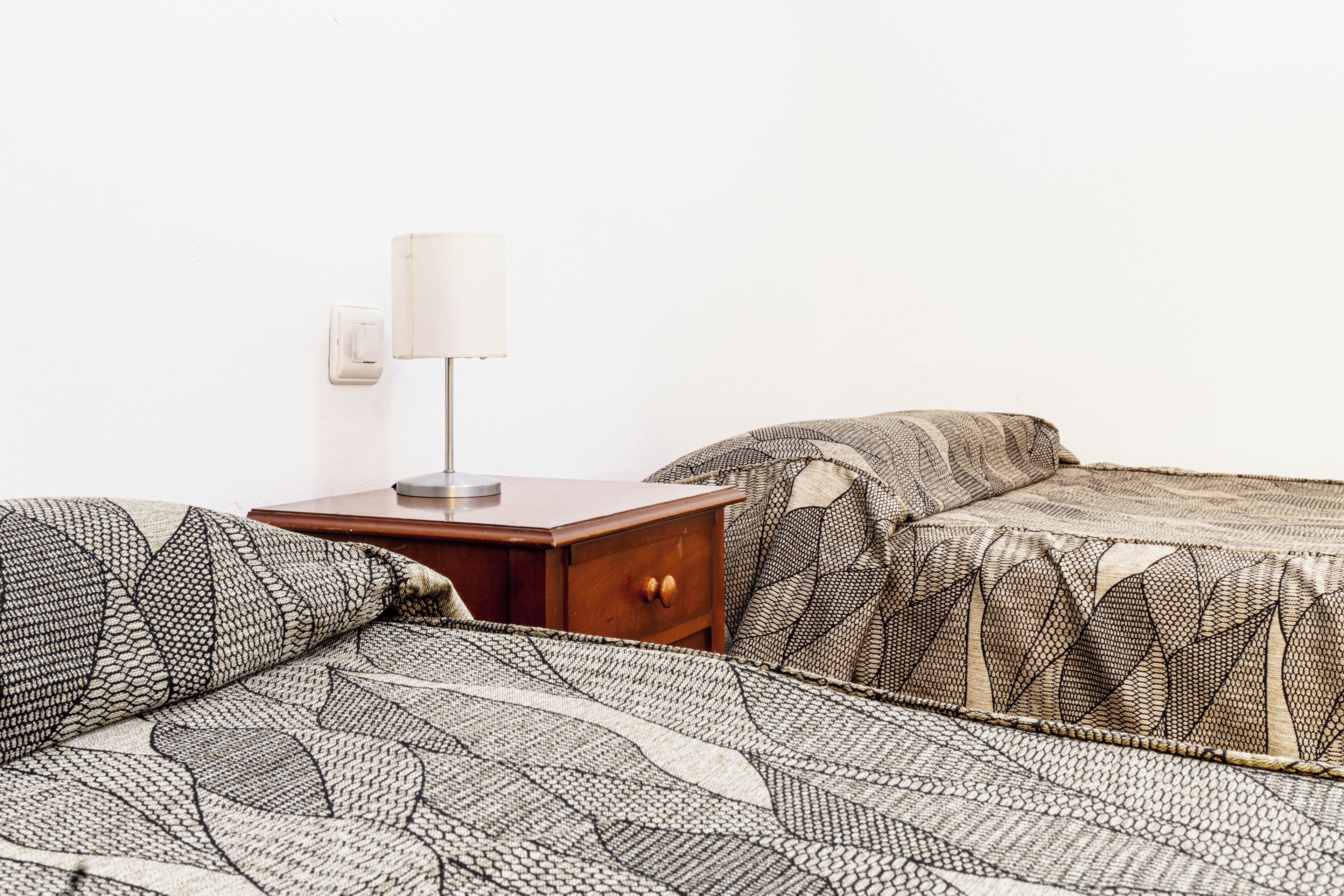 Una cama bien tendida con una colcha estampada y una mesita de noche con una lámpara.
