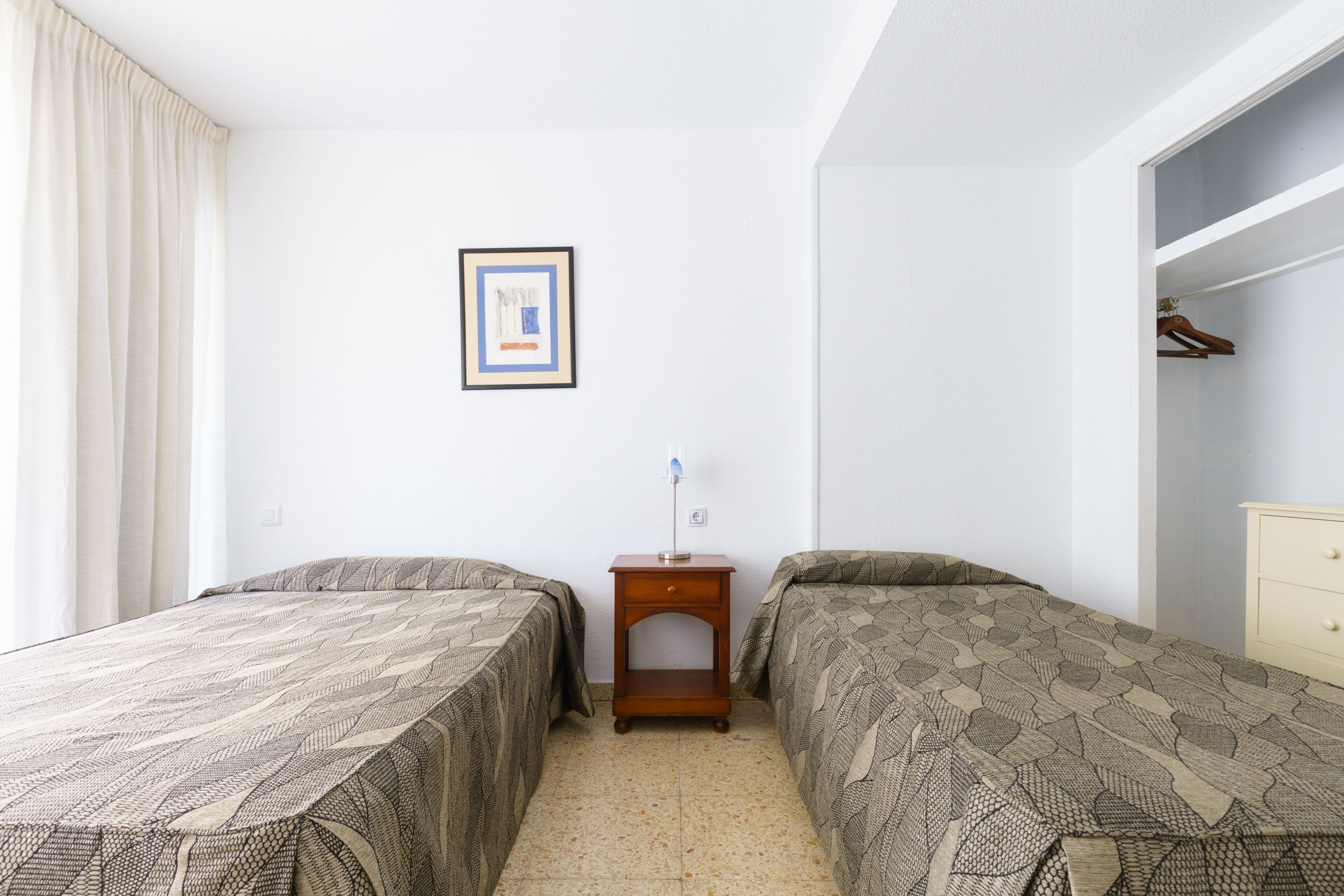 Ein Schlafzimmer mit zwei Betten, einem Nachttisch, einem gerahmten Bild an der Wand und einem Kleiderschrank.