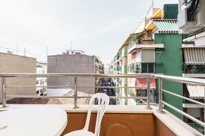 A balcony with a white chair and a table, overlooking a narrow street with colorful buildings. - Apartamentos Maja (Benidorm)