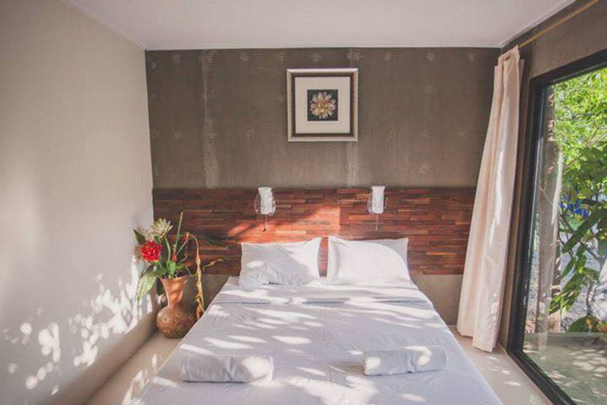 Un dormitorio moderno con una cama grande, un cabecero de madera, un cuadro enmarcado en la pared y una ventana con cortinas.