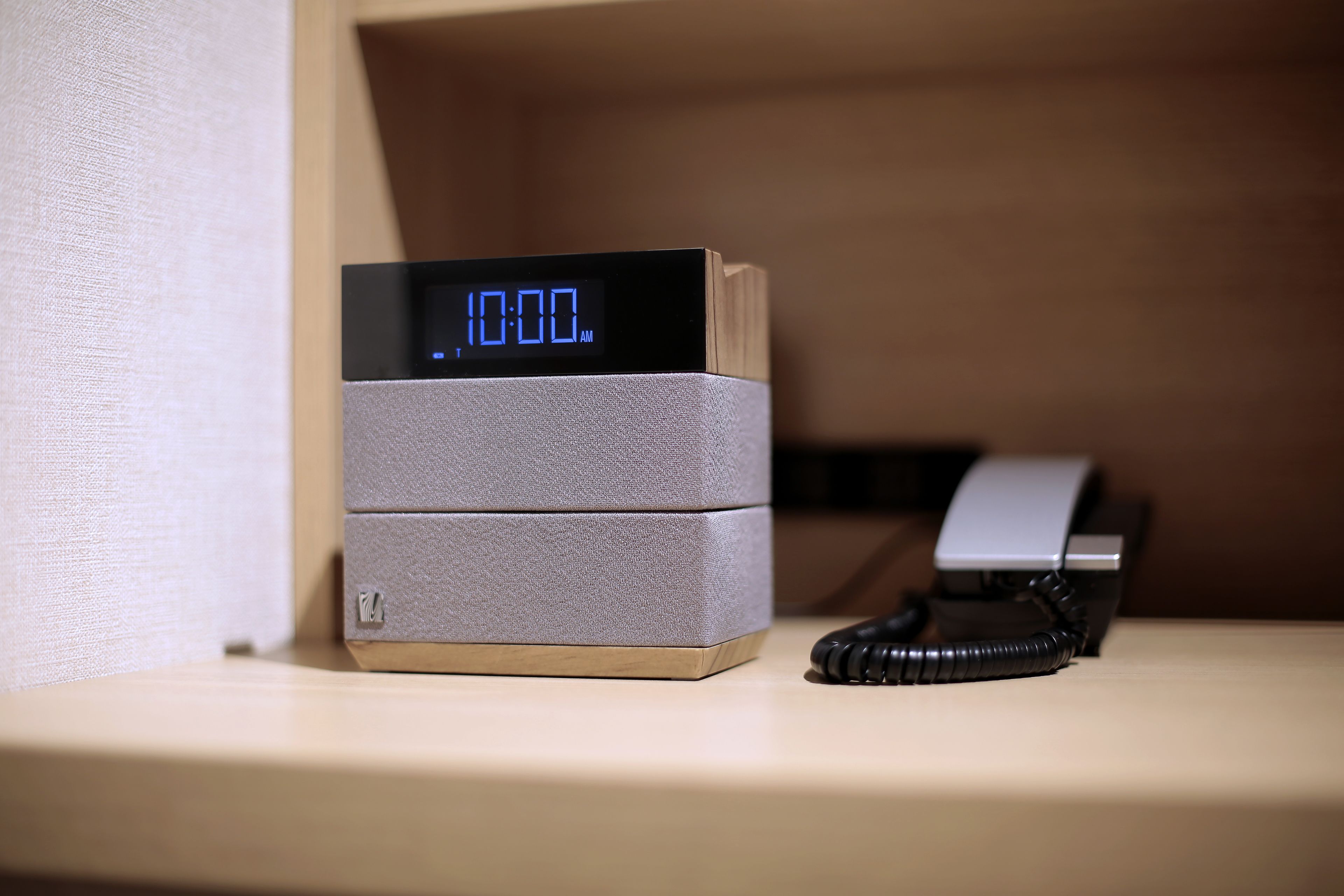 A digital clock displaying 10:00 AM on a bedside table with a telephone.