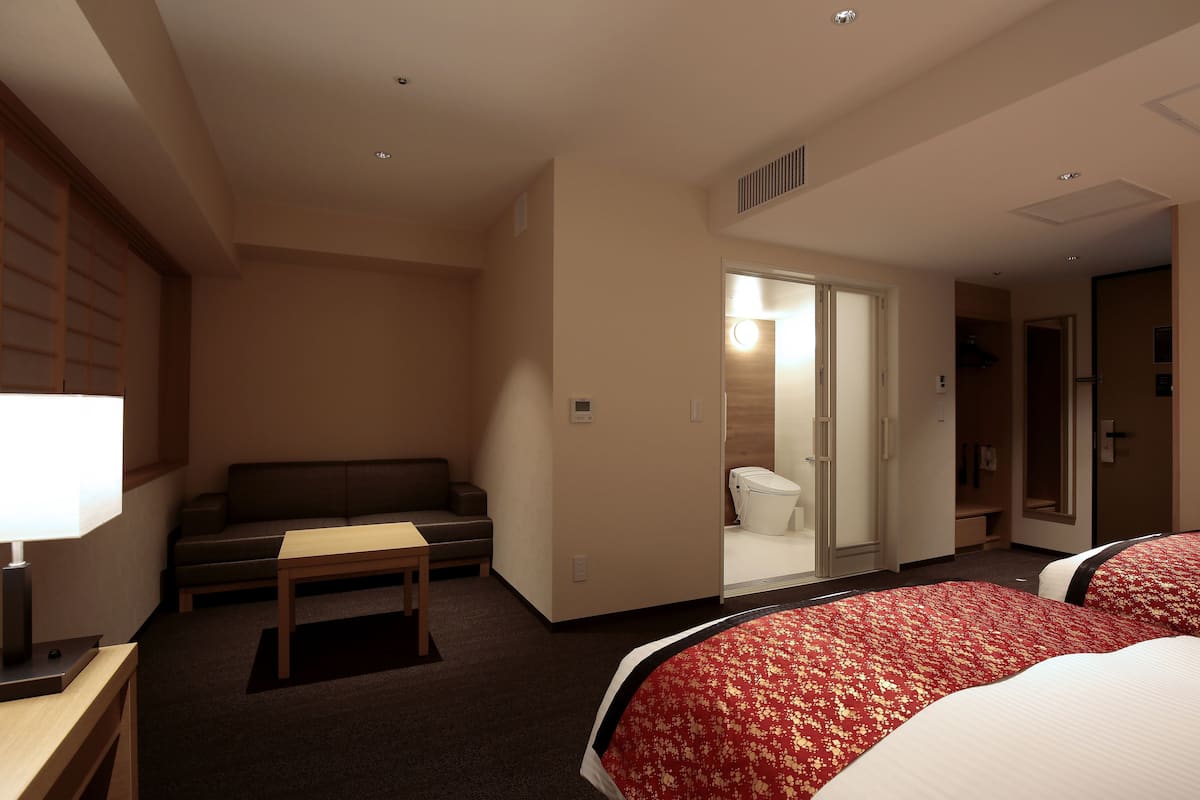 Una habitación de hotel con dos camas, un sofá, una mesa y una lámpara.