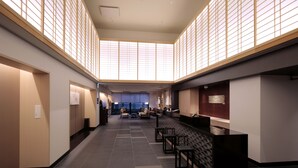 A spacious lobby with a high ceiling, large windows, and a seating area with tables and chairs.