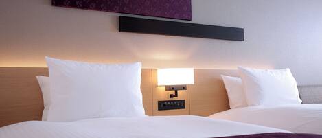 Une chambre d’hôtel avec deux lits, une table de chevet avec une lampe et un panneau fixé au mur au-dessus des lits.