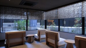 A modern interior with seating arrangements, large windows, and a view of an outdoor garden.