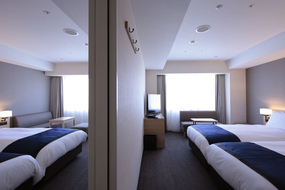 Habitación de hotel con dos camas, un escritorio, una silla, un televisor y una ventana con cortinas.