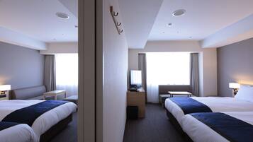 A hotel room with two beds, a desk, a chair, a TV, and a window with curtains.