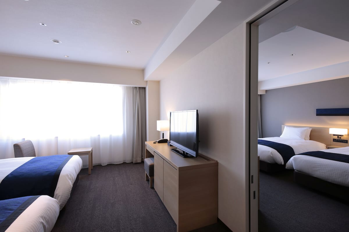 Habitación de hotel con dos camas, un escritorio con televisor y un espejo grande en una pared.