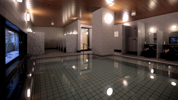 A modern indoor swimming pool with a tiled floor, wooden ceiling, and wall-mounted lights.