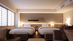 A modern hotel room with two beds, a sofa, a coffee table, and a desk.