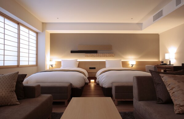 A modern hotel room with two beds, a sofa, a coffee table, and a desk.
