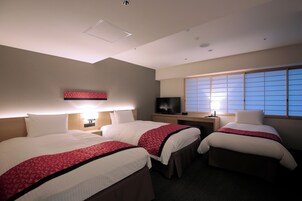 Ein Hotelzimmer mit zwei Betten, einem Fernseher, einem Fenster mit Jalousien und einem Nachttisch mit Lampe.