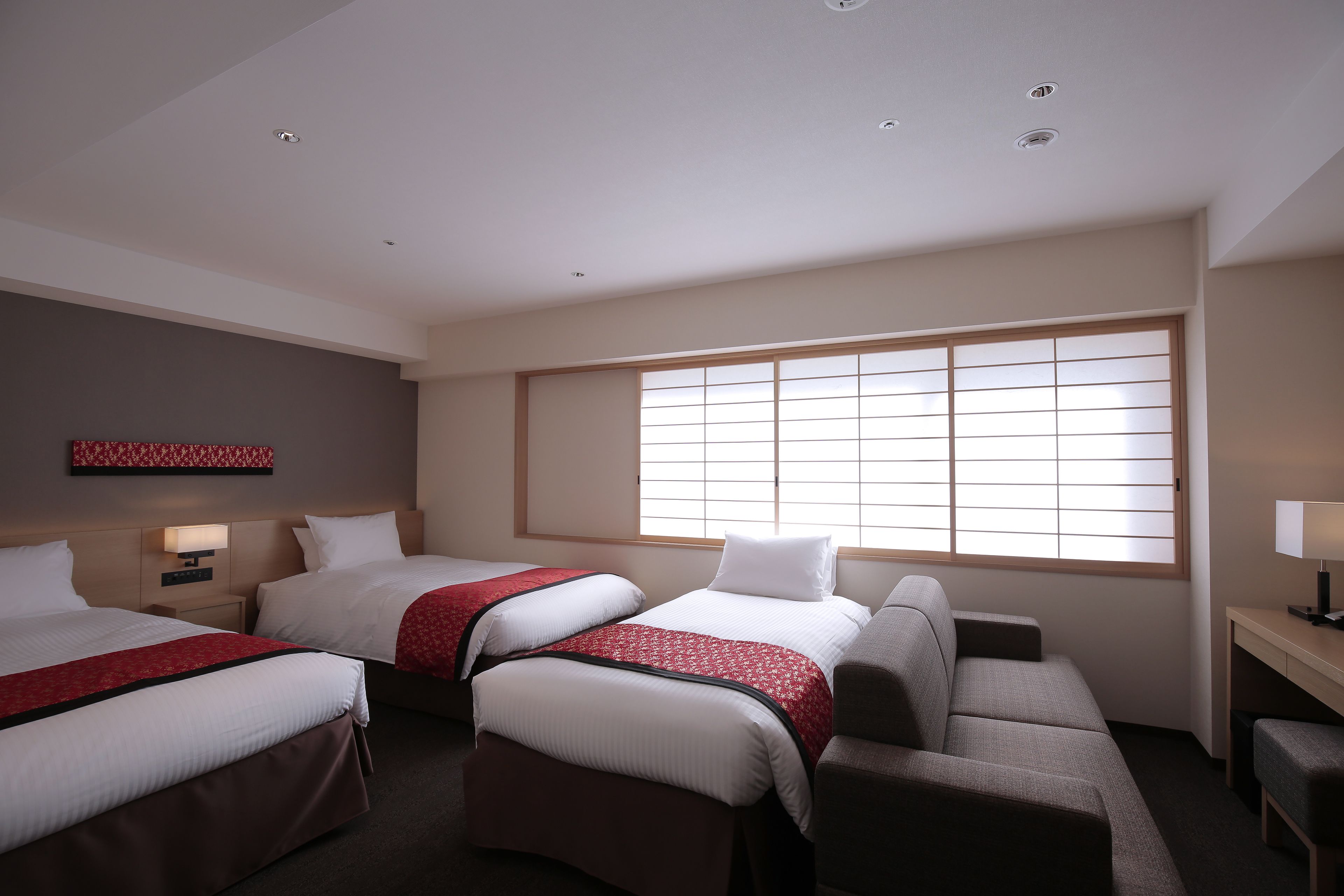 A hotel room with two beds, a sofa, a desk, and a large window.