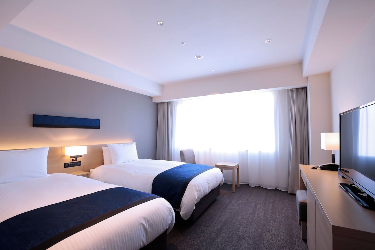 Habitación de hotel con dos camas, un escritorio, un televisor y una ventana con cortinas.