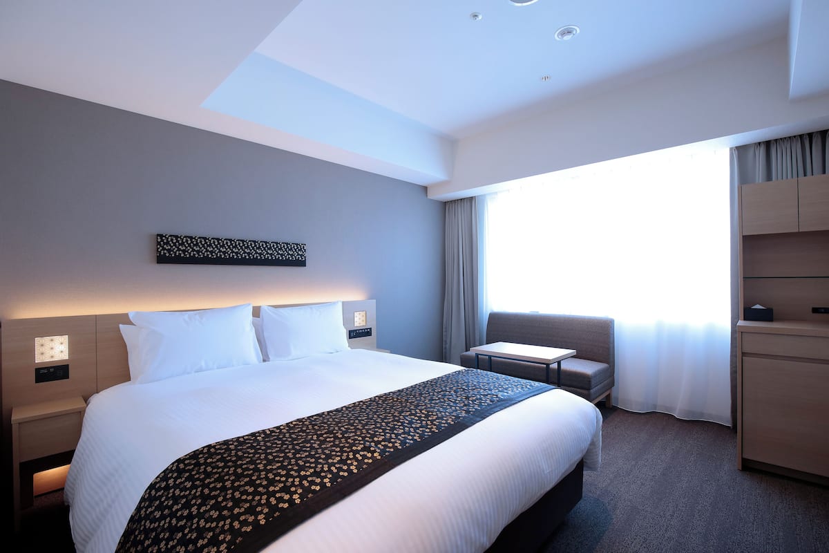 Habitación de hotel con una cama grande, un escritorio, una silla, un armario y una ventana con cortinas.