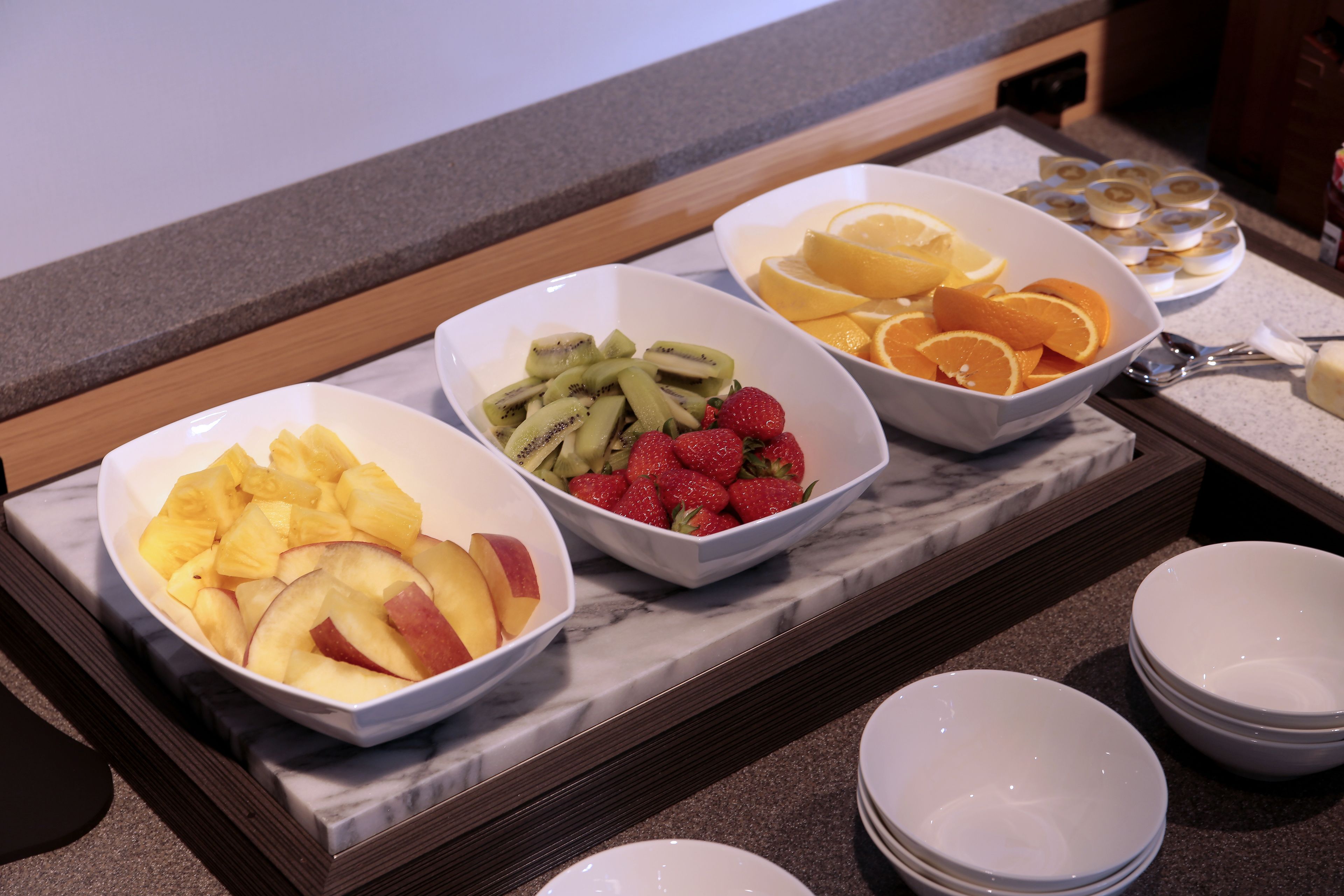 Un bufé de desayuno con tazones de piña, kiwi, fresas y naranjas.