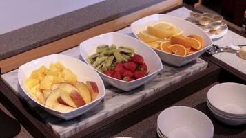 Un bufé de desayuno con tazones de piña, kiwi, fresas y naranjas.
