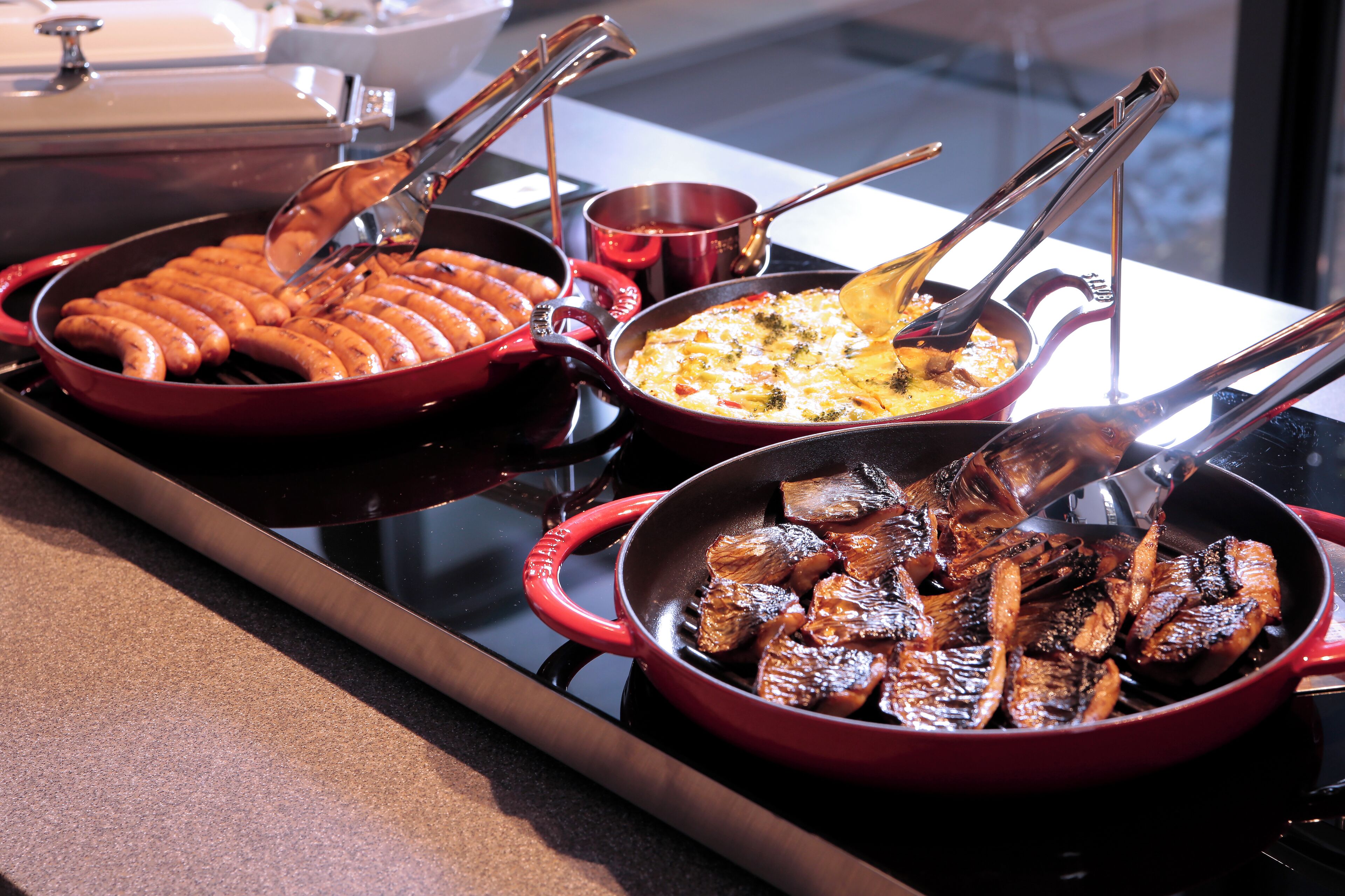 Ein Buffet mit verschiedenen Speisen, darunter Wurst, Auflauf und gegrilltes Fleisch.