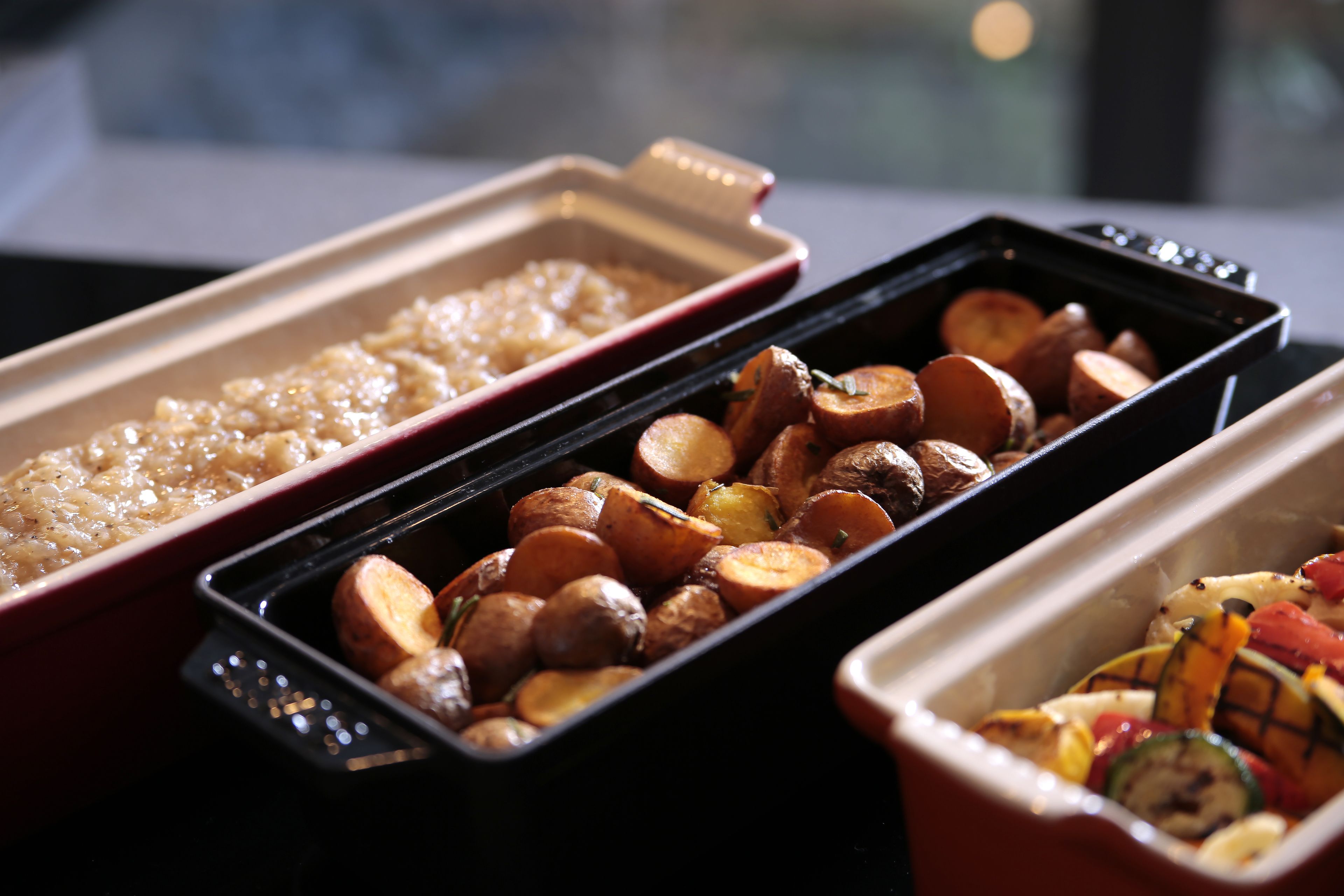 Three trays of food, including roasted potatoes, rice, and grilled vegetables.