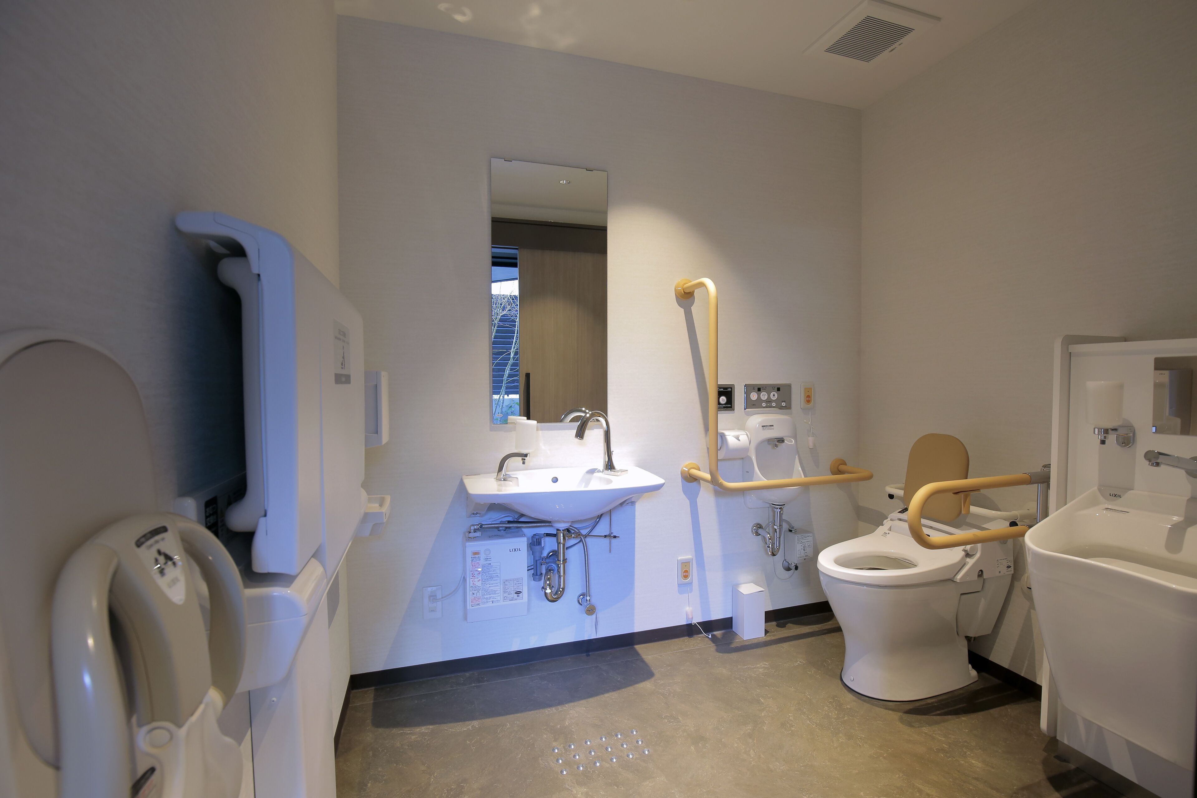 A modern bathroom with a sink, toilet, and hand sanitizer dispenser.