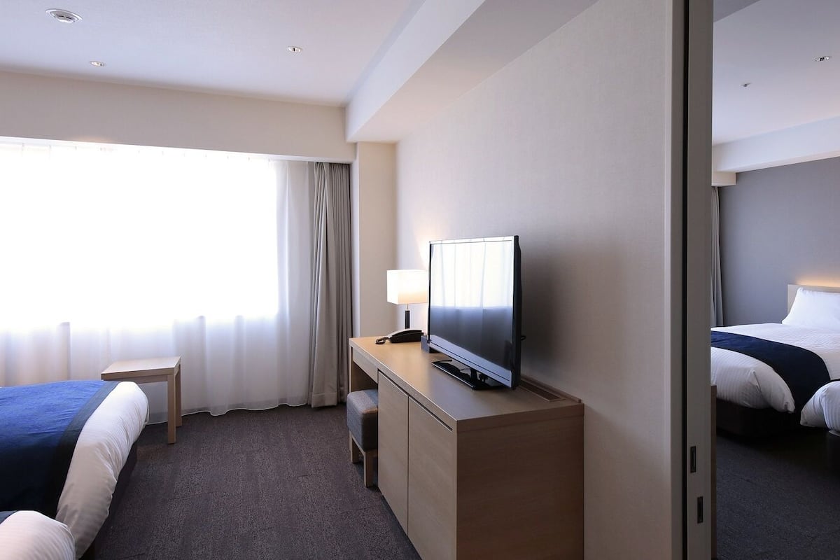 Habitación de hotel con dos camas, un escritorio, un televisor, un espejo y una ventana con cortinas.