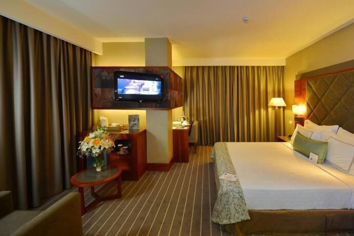 A hotel room with a large bed, a desk, a television, and a small table with a vase of flowers.