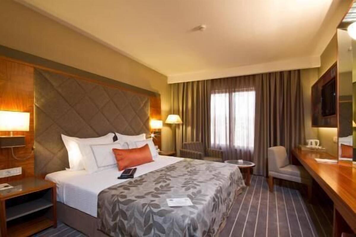 A hotel room with a bed, bedside tables, a chair, a desk, a television, and a window with curtains.
