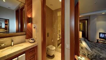 A hotel room with a wooden vanity, a large mirror, a bed with a floral bedspread, and a television on a stand.