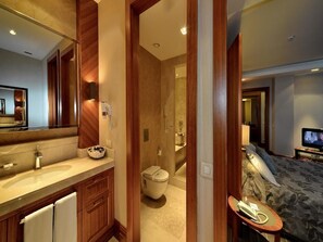 Habitación de hotel con tocador de madera, un espejo grande, cama con colcha floral y televisor sobre un soporte.