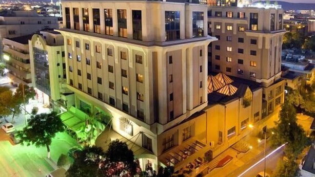Un hotel de varios pisos con un diseño arquitectónico moderno, que presenta una torre central destacada y una fachada bien iluminada.