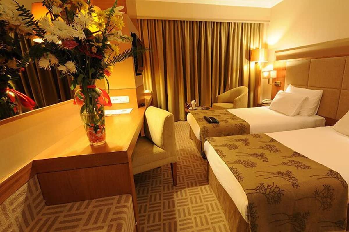 A hotel room with two beds, a desk, a chair, a vase of flowers, and a curtain.