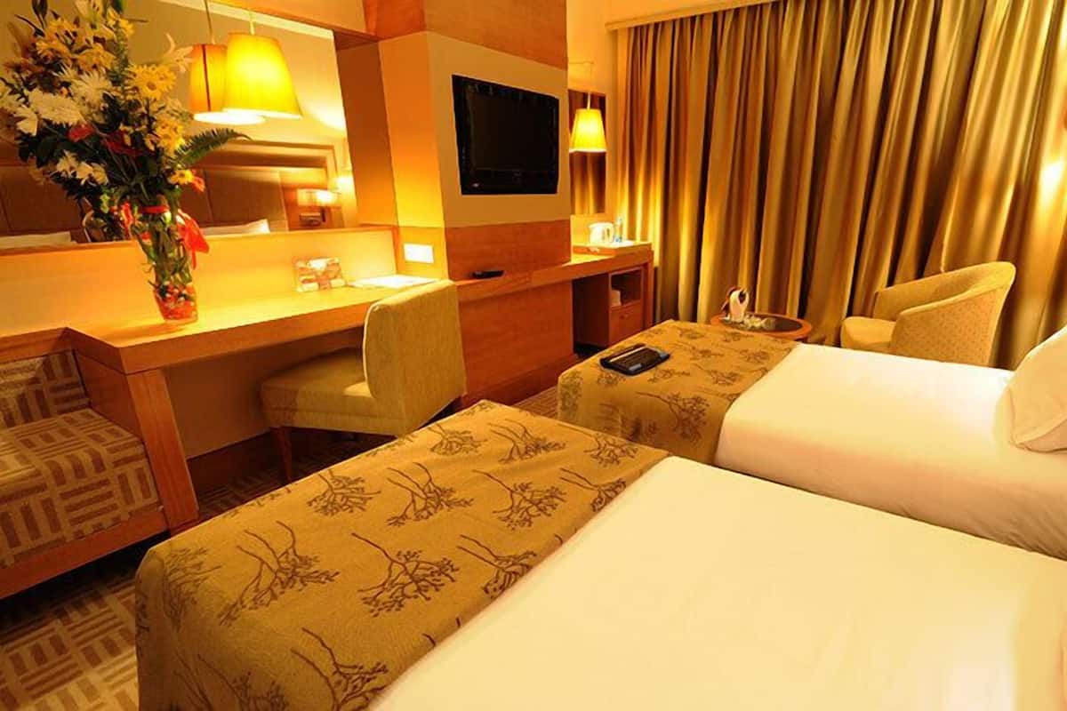 A hotel room with two beds, a desk, a chair, a TV, and a window with curtains.