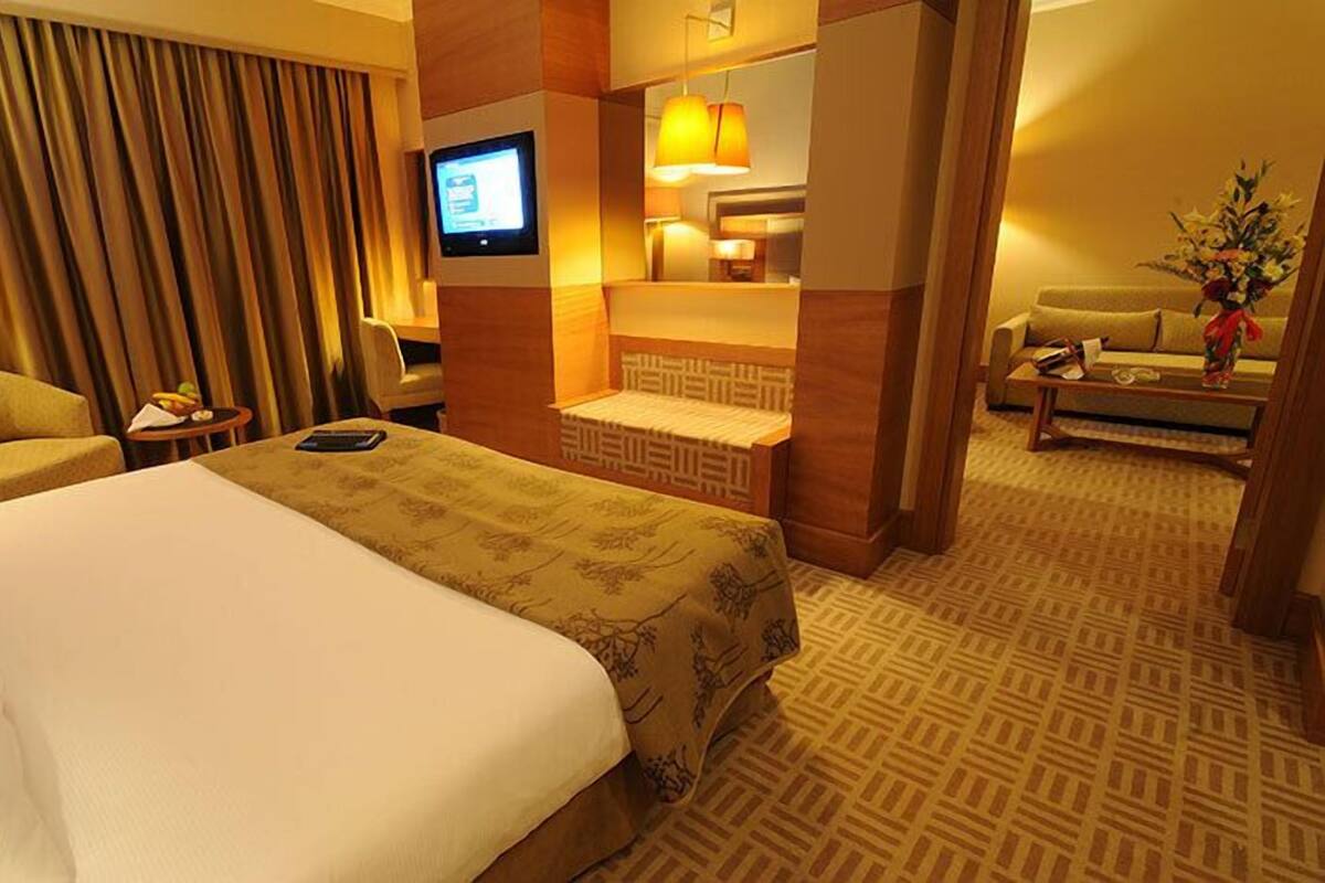 A hotel room with a large bed, a desk, a chair, a television, and a small table with a vase of flowers.