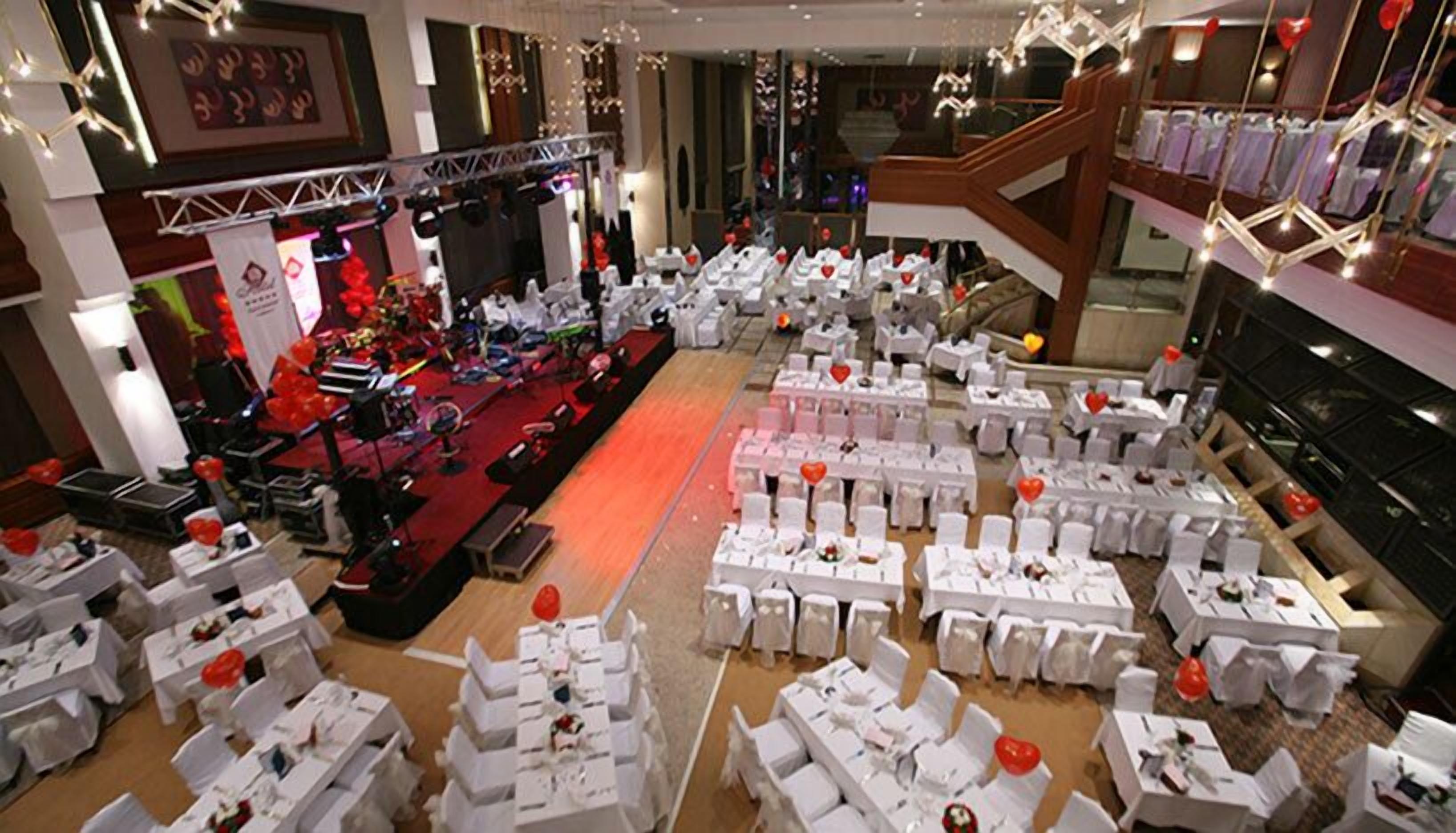 Een feestzaal met rijen tafels gedekt voor een formeel evenement, een podium met verlichting en een trap.