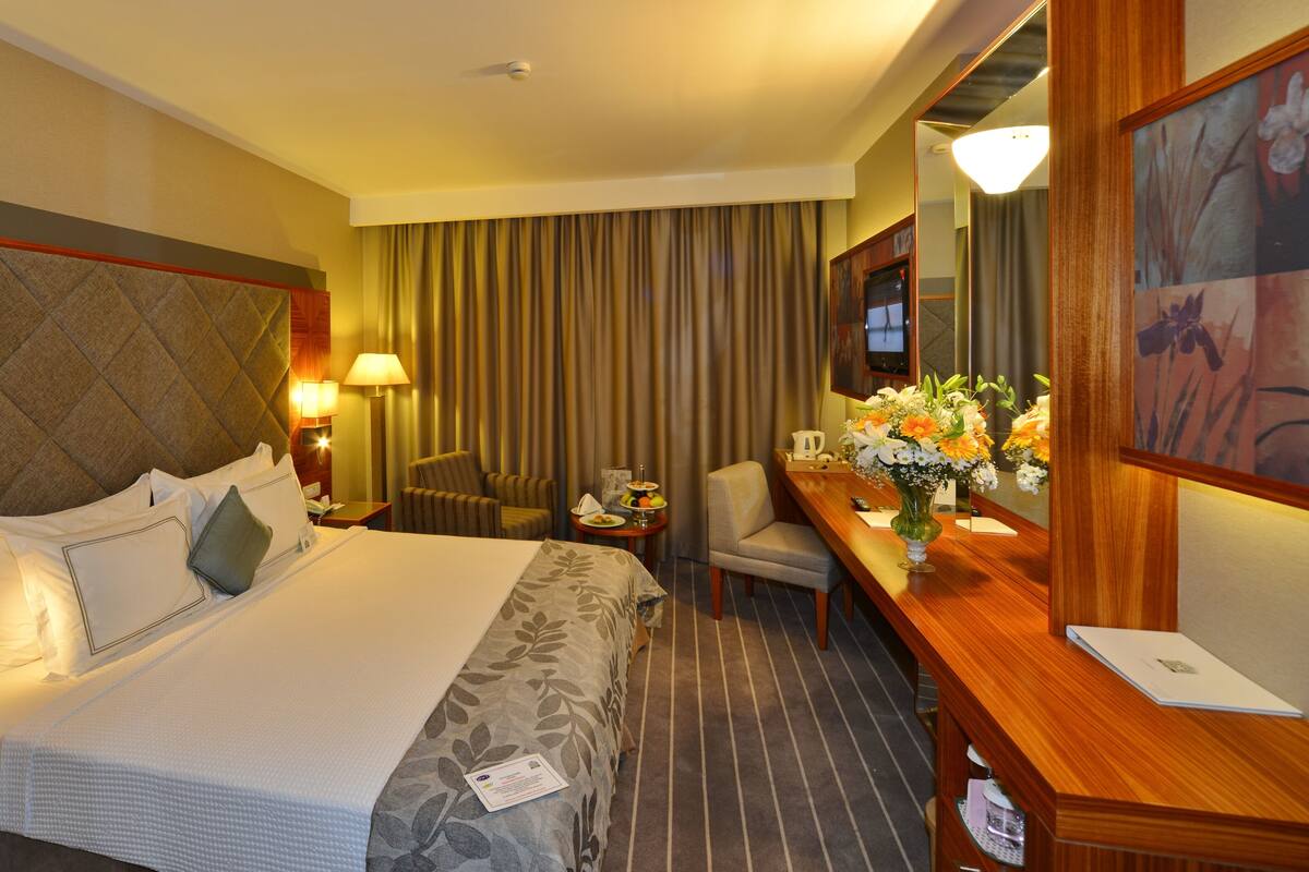 A hotel room with a large bed, a desk, a chair, a TV, and a mirror.