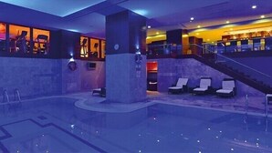 Una piscina interior moderna con sillones de descanso, una escalera y un área de bar.