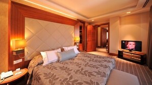 Una habitación de hotel con una cama grande, televisión, mesita de noche con teléfono y una lámpara de pared.