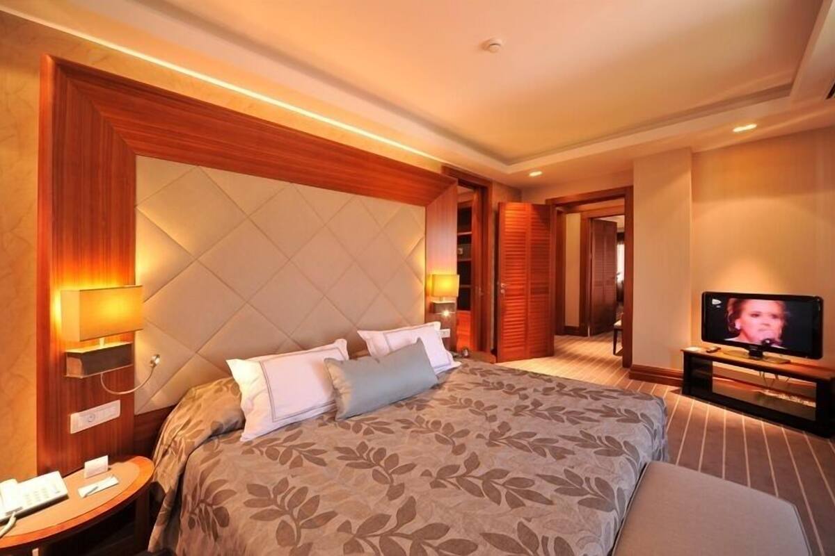 A hotel room with a large bed, a television, a bedside table with a phone, and a wall-mounted lamp.