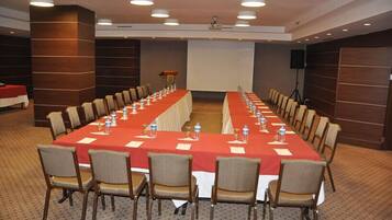 Un salón de conferencias con una larga mesa, sillas y una pantalla para proyector.