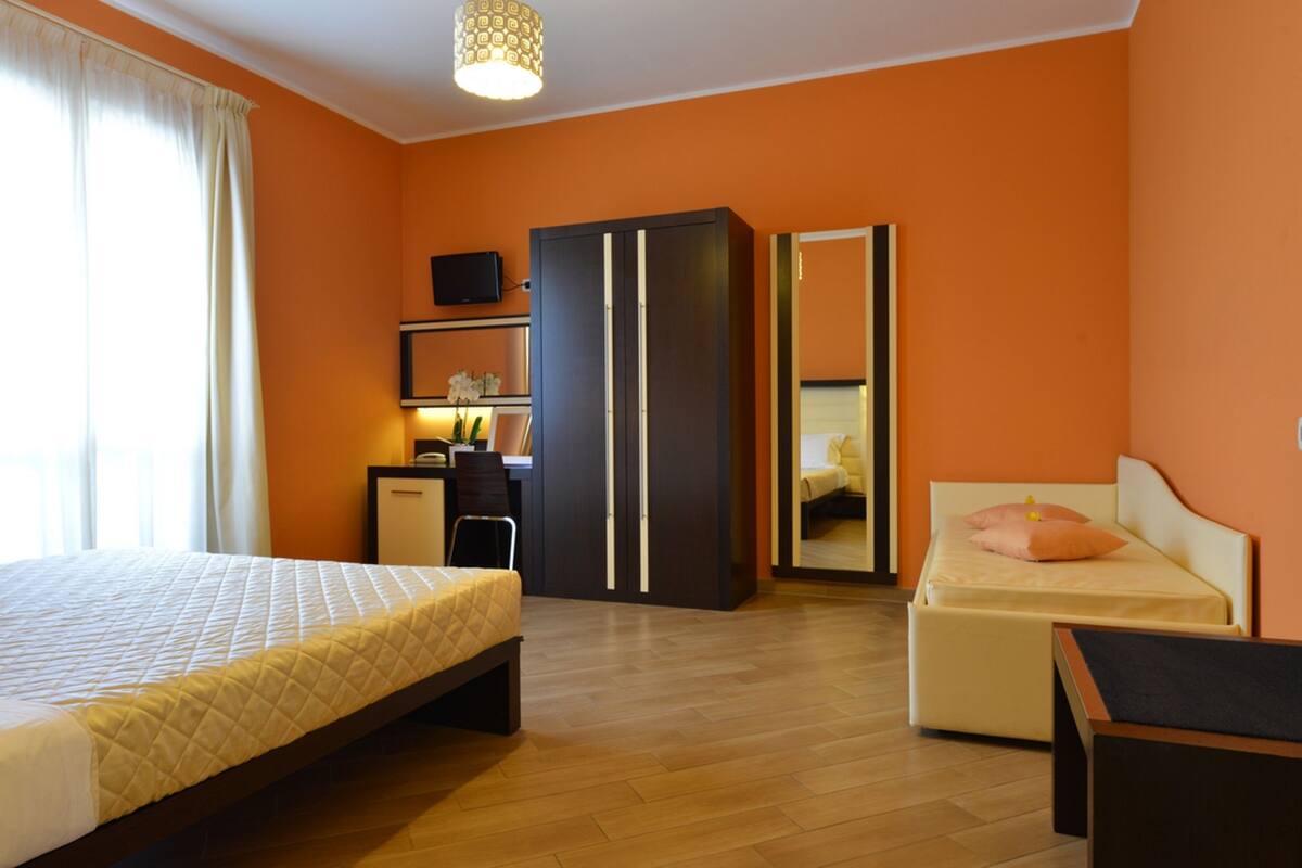 A bedroom with a bed, a desk, a wardrobe, and a mirror.