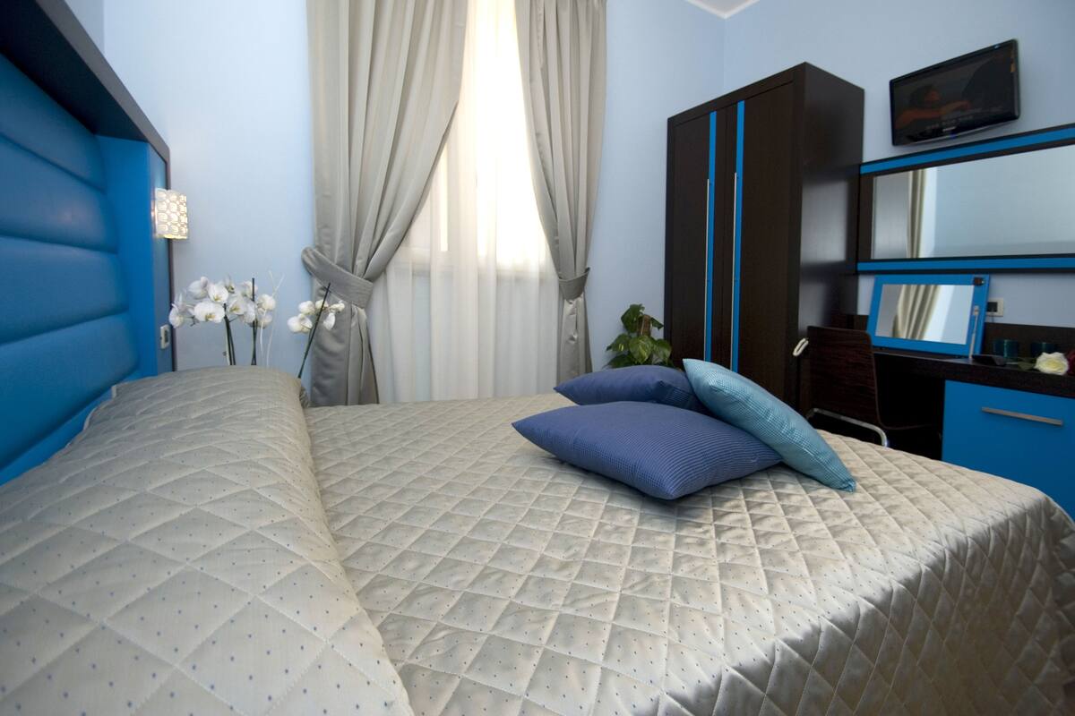 A bedroom with a bed, a wardrobe, a television, and a desk.