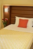 Habitación de hotel con una cama, una mesita de noche y un florero con rosas rojas.