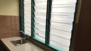 A kitchen with a stainless steel sink and a window with blinds. - Maha Hotel (Puchong)