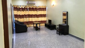 A living room with a sofa, TV, and a small table. - Maha Hotel (Puchong)