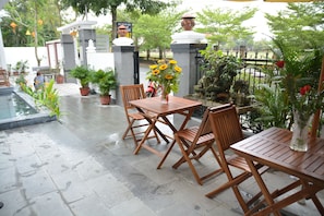 An outdoor patio with wooden tables and chairs, surrounded by potted plants and a decorative fountain. - Horizon 2 Villa Hoi An (Da Nang)