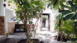 A narrow pathway flanked by potted plants and a small garden area with a brick wall and a wooden bench. - Padanta Homestay (Gili Trawangan)