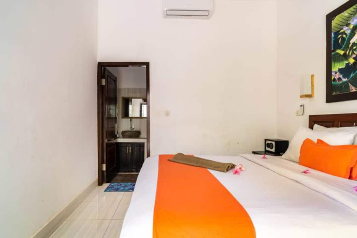 A hotel room with a bed, a nightstand, a radio, and a painting on the wall.