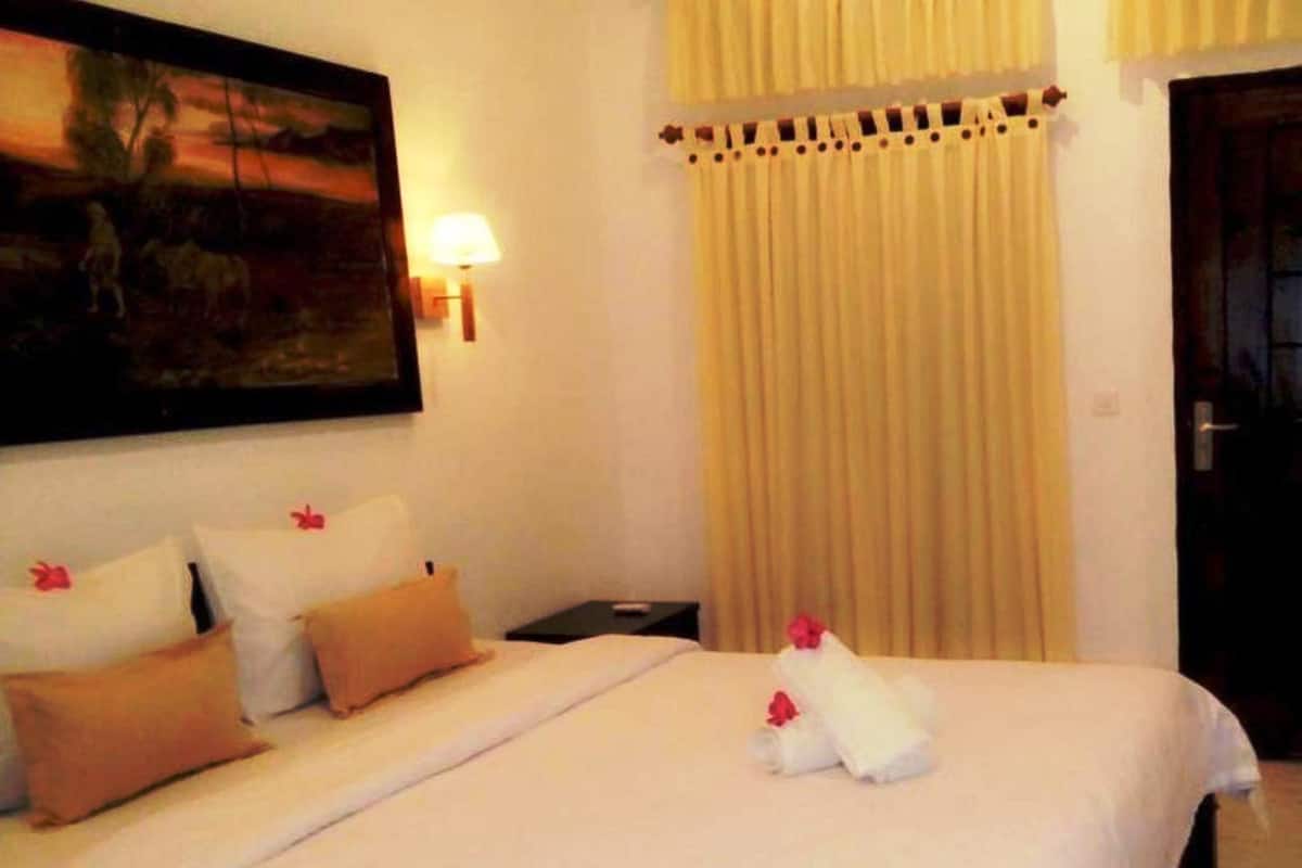 A hotel room with a bed, pillows, a nightstand, a lamp, and a painting on the wall.
