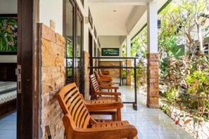 A covered outdoor seating area with wooden benches and a stone wall. - Padanta Homestay (Gili Trawangan)